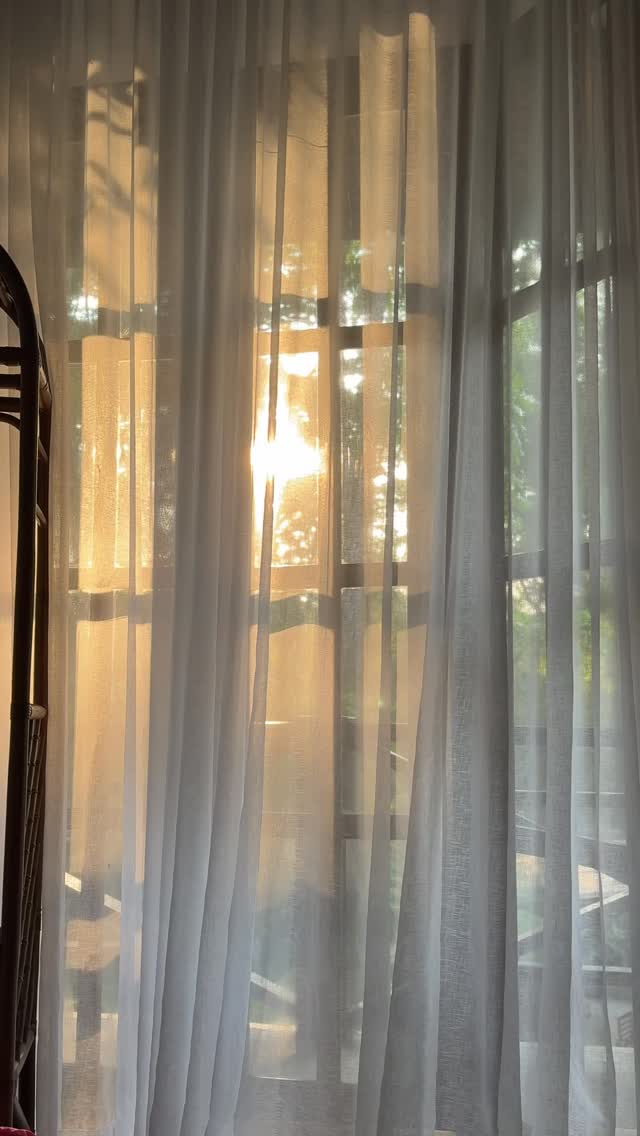 Sheer curtains billow in warm golden sunrise light inside a heritage bedroom at The Red Hen Homestead